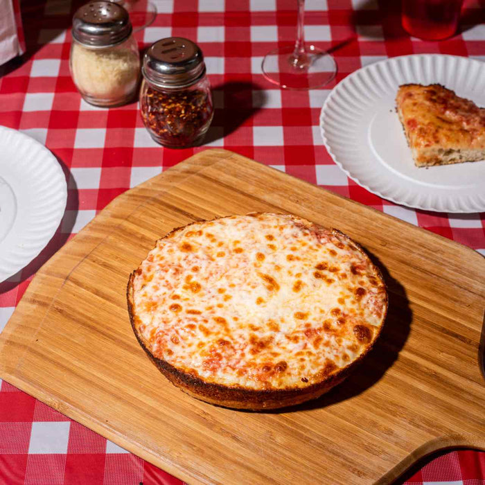 Cooked pan pizza with tomato sauce and mozzarella on an Ooni Bamboo Peel & Serving Board on a table with plates of slices of pan pizza.